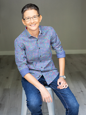 Jen sits on casually on a stool, smiling at the camera.