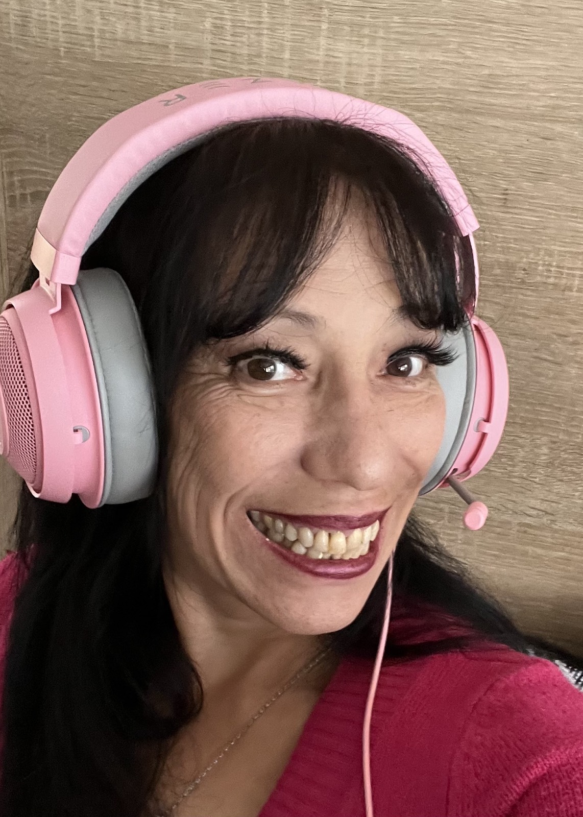 A woman with dark hair, wearing pink headphones smiles brightly at the camera.