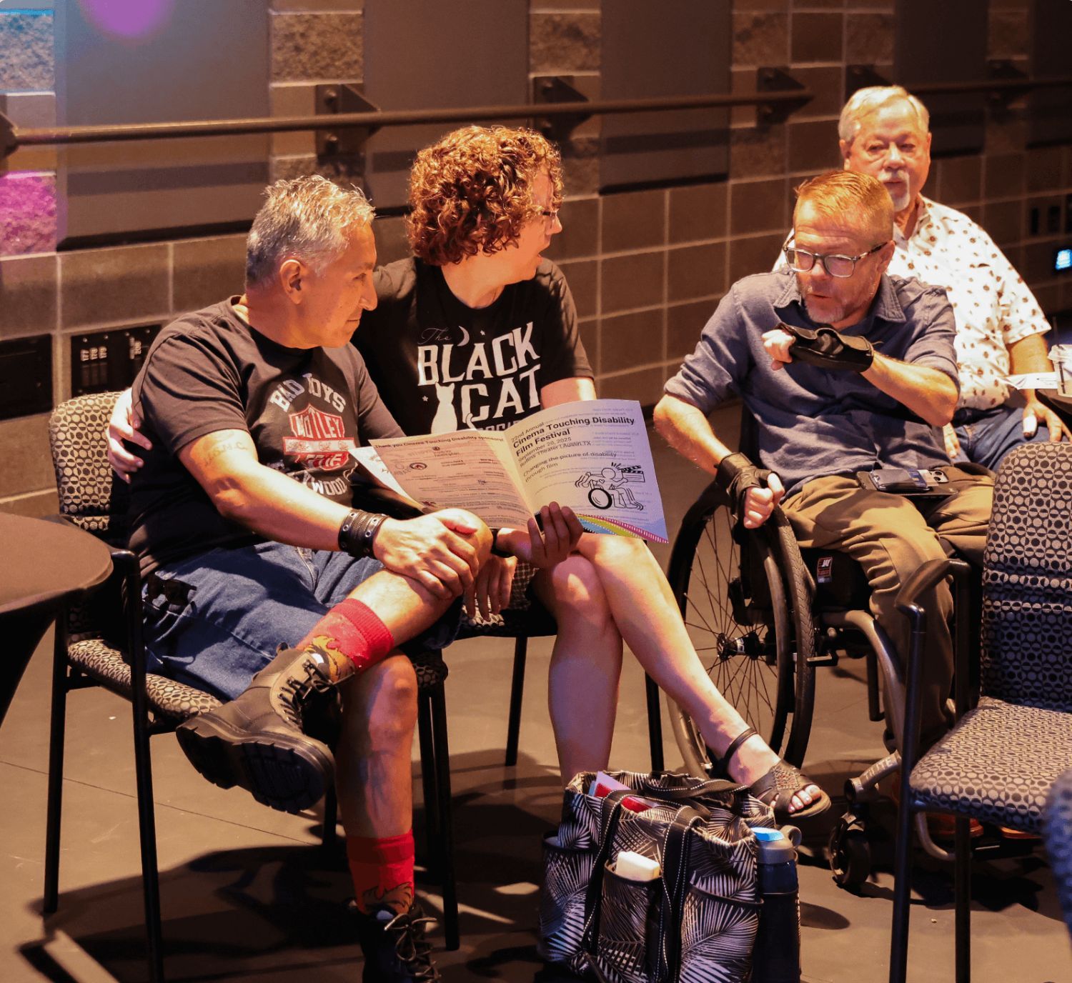 A white wheelchair user speaks animatedly to two other white fest attendees during a moment between films